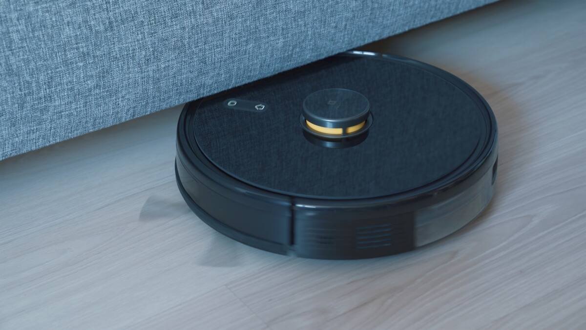 Black robot vacuum cleaning a wooden floor