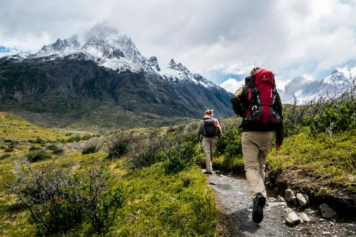 Two hikers with backpacks walking toward snow-capped mountains