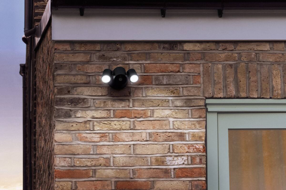 Floodlight camera mounted above a door on a brick wall, lit at night