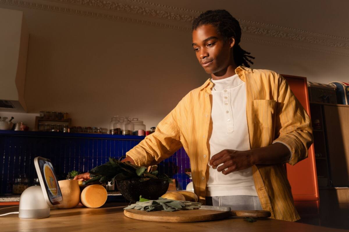 A person cooking in a kitchen glances at an Apple HomeView on the counter